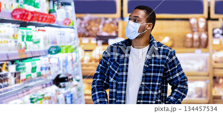 Young black guy in disposable face mask selecting dairy products at store during covid quarantine. African American man shopping for fresh food products at mall or supermarket Young black guy in disposable face mask selecting dairy products at store during covid quarantine. African American man shopping for fresh food products at mall or supermarket 134457534