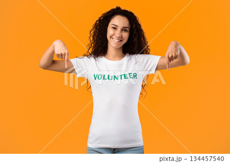 Cheerful Volunteer Lady Pointing Fingers Down Smiling To Camera Posing Standing Over Yellow Studio Background. Activist Advertising Something. Look There, Volunteering Advertisement 134457540