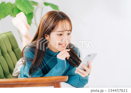 ソファに寝転がってスマホを使う女性 134457621