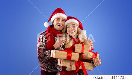 Romantic millennial couple with pile of Xmas gifts hugging and smiling on blue background Romantic millennial couple with pile of Xmas gifts hugging and smiling on blue background 134457833