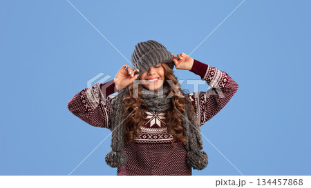 Winter outfit. Millennial woman pulling down knitted beanie hat and smiling on blue background, panorama Winter outfit. Millennial woman pulling down knitted beanie hat and smiling on blue background, panorama 134457868