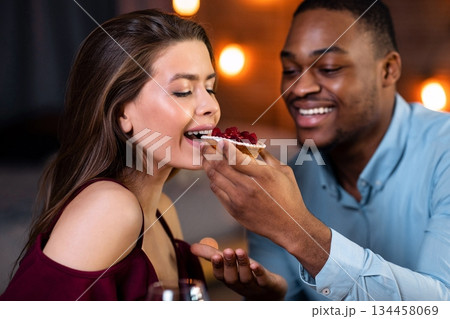 Cheerful Interracial Couple Enjoying Sharing Dessert Together During Romantic Date In Restaurant, Loving African American Man Feeding His Happy Girfriend, Multicultural Lovers Enjoying Dinner Cheerful Interracial Couple Enjoying Sharing Dessert Together During Romantic Date In Restaurant, Loving African American Man Feeding His Happy Girfriend, Multicultural Lovers Enjoying Dinner 134458069