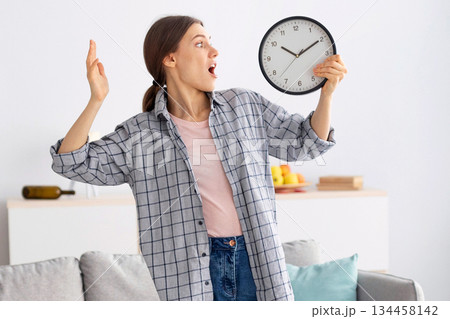 Shocked young woman holding clock, feeling terrified, standing in messy room after party, being late to clean apartment, copy space. Millennial maid not meeting cleanup deadline Shocked young woman holding clock, feeling terrified, standing in messy room after party, being late to clean apartment, copy space. Millennial maid not meeting cleanup deadline 134458142