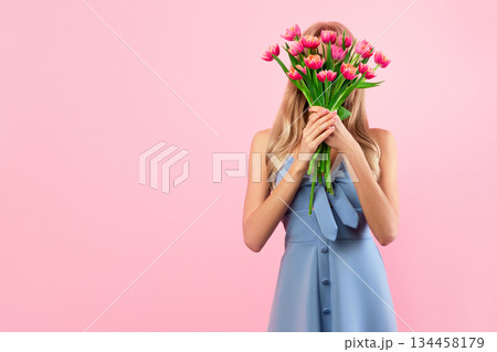 Full length portrait of unrecognizable young lady covering face with bouquet of spring flowers on pink studio background, copy space. Faceless blonde in dress holding tulips, celebrating Woman's Day Full length portrait of unrecognizable young lady covering face with bouquet of spring flowers on pink studio background, copy space. Faceless blonde in dress holding tulips, celebrating Woman's Day 134458179