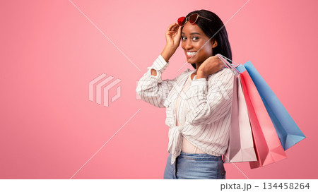 Gorgeous young woman with shopping bags smiling and looking at camera on pink studio background. Pretty black lady buying gifts for holiday, happy over big discounts 134458264