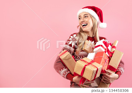 Lovely Caucasian woman in Xmas outfit holding stack of wrapped Christmas gifts on pink studio background. Pretty millennial lady shopping for festive season. Holiday sale concept Lovely Caucasian woman in Xmas outfit holding stack of wrapped Christmas gifts on pink studio background. Pretty millennial lady shopping for festive season. Holiday sale concept 134458306