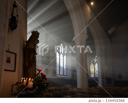 Norwich, Norfolk, UK: Church interior with a statue of Mary and Jesus. Sunlight streams through the windows. Candles and flowers complete the scene. 134458366