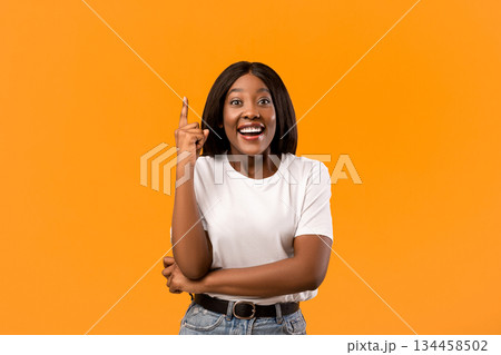 Inspiration, creativity, solution, eureka concept. Inspired young black woman in white t-shirt raising finger up and smiling, having creative idea, orange studio background, copy space Inspiration, creativity, solution, eureka concept. Inspired young black woman in white t-shirt raising finger up and smiling, having creative idea, orange studio background, copy space 134458502