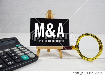 M and A abbreviation of Mergers Acquisitions text with magnifying glass and calculator on wooden background M and A abbreviation of Mergers Acquisitions text with magnifying glass and calculator on wooden background 134458794