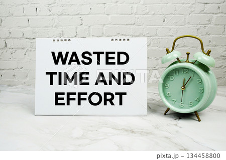 Wasted Time and Effort with green vintage alarm clock against a white brick wall background 134458800