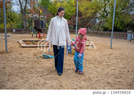 Mother and daughter holding hands and walking together in a sandy playground. Quality time and peaceful moments in autumn. Mother and daughter holding hands and walking together in a sandy playground. Quality time and peaceful moments in autumn. 134458910