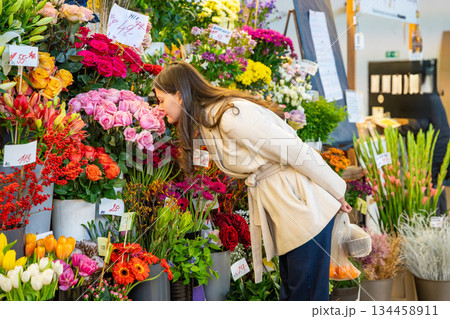 Woman smelling colorful flowers at an outdoor flower stall. Connection with nature through senses. 134458911