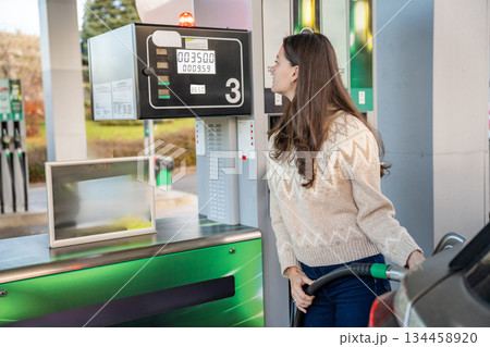 Woman standing next to a fuel dispenser at a gas station. Personal transportation and daily errands. 134458920