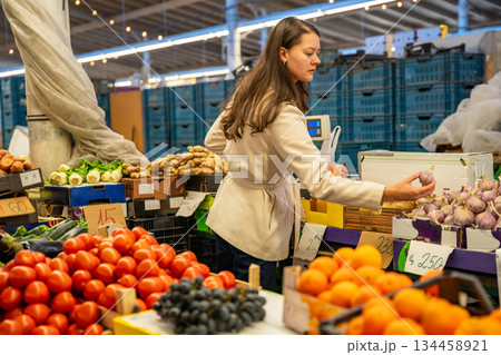 Woman choosing onions at a fruit and vegetable market indoors. Shopping habits and conscious food choices. Woman choosing onions at a fruit and vegetable market indoors. Shopping habits and conscious food choices. 134458921
