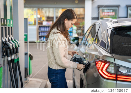 Woman filling up her car with gasoline at a gas station. Routine task during a road trip or commute. 134458957