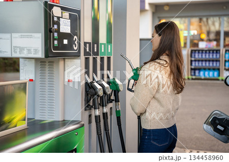 Back view of woman preparing to pump fuel into her car. Routine car maintenance at gas station. Back view of woman preparing to pump fuel into her car. Routine car maintenance at gas station. 134458960