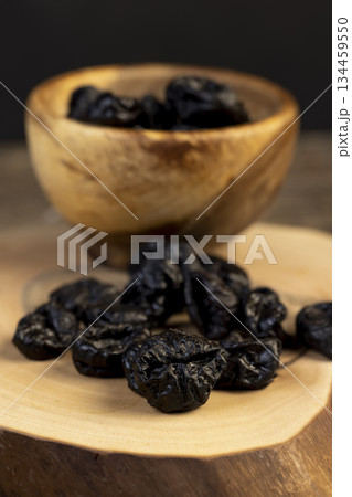 black soft dehydrated fruits of plums, prunes scattered on the kitchen table, black sweet seedless prunes scattered on the table 134459550