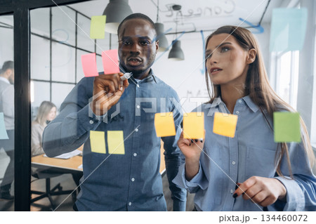 Paper stickers on the glass. Professional workers are in the modern office together Paper stickers on the glass. Professional workers are in the modern office together 134460072