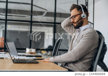 In headphones. Man is sitting in the office by the laptop, conception of business In headphones. Man is sitting in the office by the laptop, conception of business 134460094