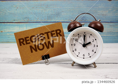 Register Now text written on paper card with alarm clock on wooden background Register Now text written on paper card with alarm clock on wooden background 134460926