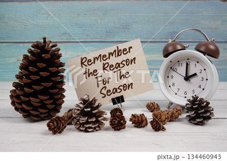 Remember the Reason For The Season text written on paper card with alarm clock and pine cones decoration on wooden background Remember the Reason For The Season text written on paper card with alarm clock and pine cones decoration on wooden background 134460943
