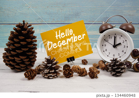 Hello December Christmas Is Coming text written on paper card with alarm clock and pine cones decoration on wooden background Hello December Christmas Is Coming text written on paper card with alarm clock and pine cones decoration on wooden background 134460948