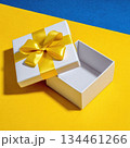 Open empty white gift box with yellow ribbon on bright blue and yellow background during festive celebration 134461266