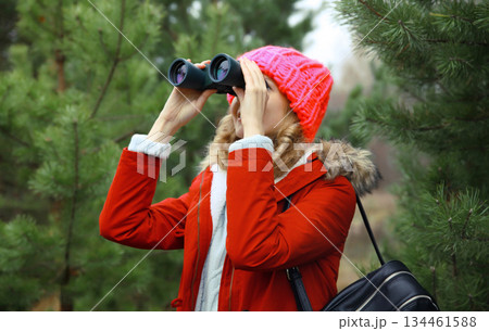 Woman tourist looking through binoculars watching nature, wild animals walking in winter forest Woman tourist looking through binoculars watching nature, wild animals walking in winter forest 134461588