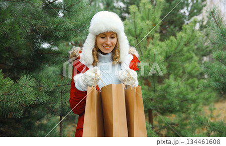 Happy smiling young woman with shopping bag in winter against Christmas tree, snow, holiday shopping 134461608
