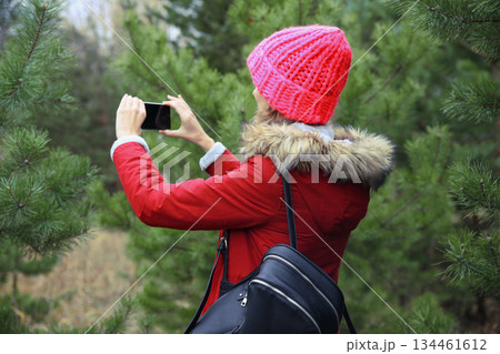 Young woman taking picture on phone Christmas tree in winter park, girl with smartphone in forest 134461612