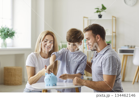 Happy Parents And Child Putting A Coin In A Piggy Bank At Home 134462146