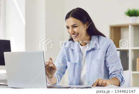 Smiling businesswoman sitting at the desk and having video call on a laptop in the office. 134462147