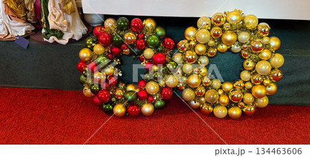 Two Christmas bauble wreaths in red green and gold placed on festive carpet. Holiday showroom atmosphere, winter decoration tradition and cheerful seasonal celebration mood Two Christmas bauble wreaths in red green and gold placed on festive carpet. Holiday showroom atmosphere, winter decoration tradition and cheerful seasonal celebration mood 134463606
