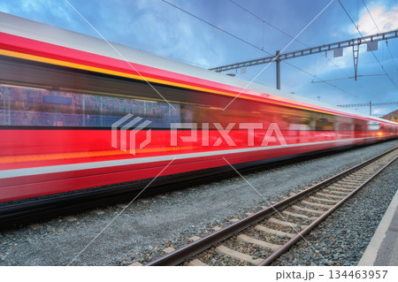 Blurred red passenger train passing mountain railway station 134463957