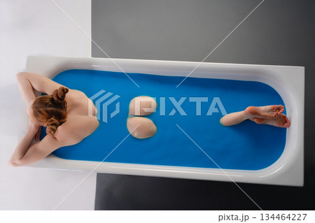 Woman relaxing in a stylish bathtub with vibrant blue water in a modern setting 134464227