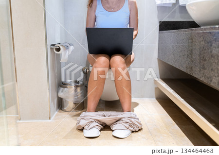 Adult woman using laptop while sitting on toilet in modern bathroom Adult woman using laptop while sitting on toilet in modern bathroom 134464468