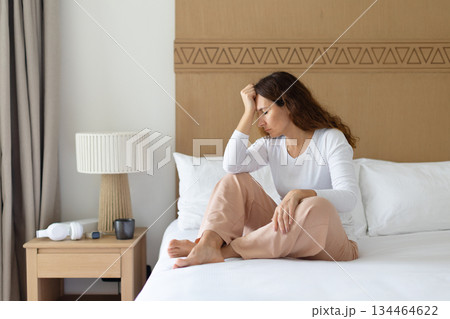 Thoughtful depressed woman sitting on bed in bedroom, resting head on hand Thoughtful depressed woman sitting on bed in bedroom, resting head on hand 134464622