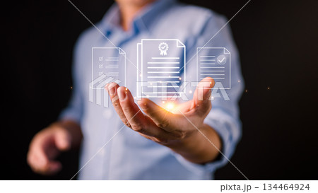 A businessman holds glowing digital document icons, representing certification, compliance, digital records, quality assurance, verified documentation, and modern data management systems. A businessman holds glowing digital document icons, representing certification, compliance, digital records, quality assurance, verified documentation, and modern data management systems. 134464924