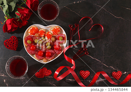 Valentine's Day treats, heart of fresh canapes with salami, caviar, cheese and grapes for buffet with roses, red wine, red hearts for the festive table, banner for advertising, invitations to the bar 134465844