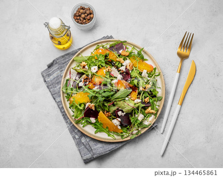 A fresh salad of beets, orange, and arugula with feta, walnuts, and balsamic dressing on a plate 134465861