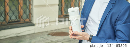 Male caucasian young adult in blue suit holding reusable coffee cup outdoors Male caucasian young adult in blue suit holding reusable coffee cup outdoors 134465896