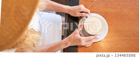 Top view of female holding cup of coffee with latte art in cafe setting 134465898