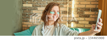 Caucasian young female enjoying morning skincare routine with eye patches while Caucasian young female enjoying morning skincare routine with eye patches while 134465900