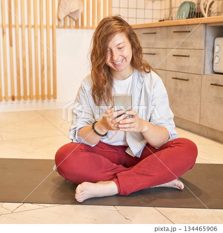 Young caucasian female relaxing on yoga mat at home using smartphone in casual Young caucasian female relaxing on yoga mat at home using smartphone in casual 134465906