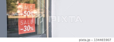 Storefront sale signs displaying 50 and 30 percent discounts on glass door 134465907