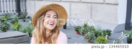 Smiling young caucasian female in straw hat enjoying outdoor garden setting 134465910