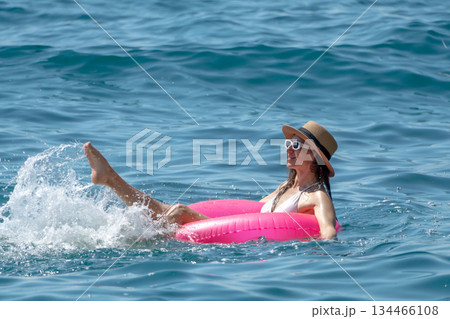 Woman Floating Water, relaxed on pink ring, splashing in blue sea, enjoying summer day vacation. 134466108
