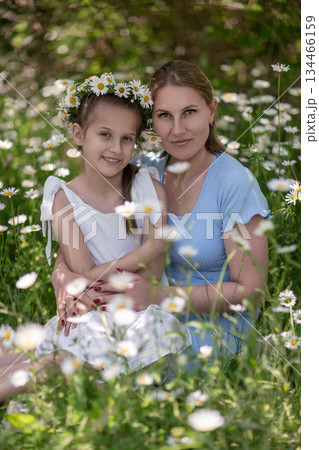 Daisies Family Portrait: Mom, daughter smiling in meadow with flower crown to celebrate family time. 134466159