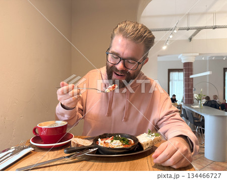 Man tasting breakfast in cafe. Connection between comfort, flavor and emotion through food, coffee and quiet morning atmosphere. Man tasting breakfast in cafe. Connection between comfort, flavor and emotion through food, coffee and quiet morning atmosphere. 134466727
