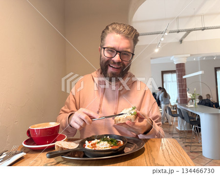Man eating breakfast in cozy cafe. Relaxed morning routine, comfort, and authentic dining experience with coffee and warm atmosphere. 134466730